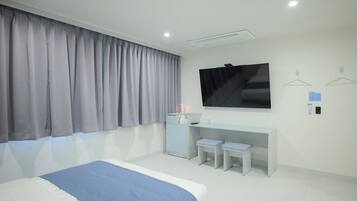 A modern hotel room with a large bed, a desk with two chairs, a flat-screen TV, and a wardrobe.