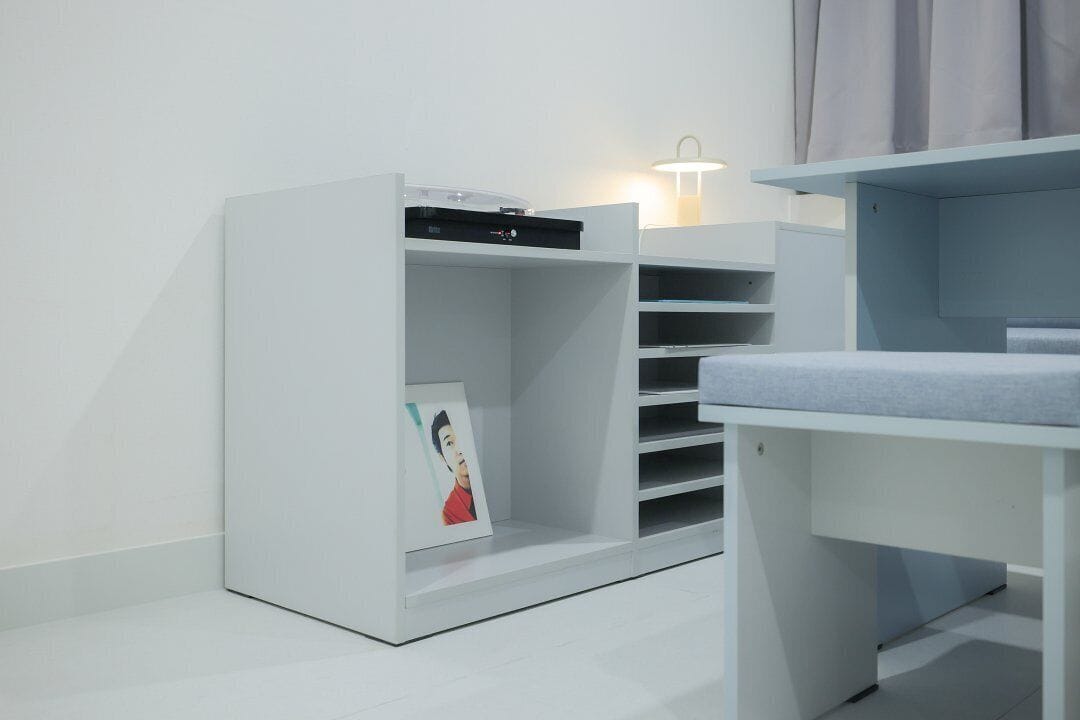 A modern, minimalist room with a white wardrobe, a desk, and a wall-mounted lamp.