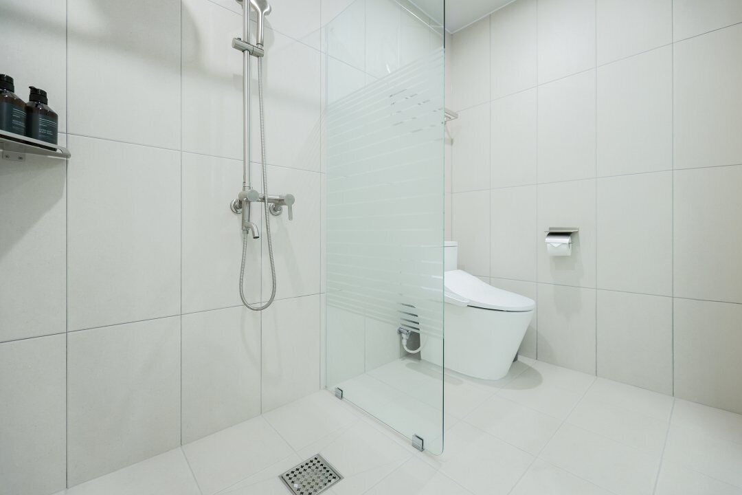 A modern bathroom with a glass-enclosed shower, a white toilet, and a shelf with toiletries.
