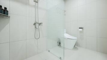 A modern bathroom with a glass-enclosed shower, a white toilet, and a shelf with toiletries.