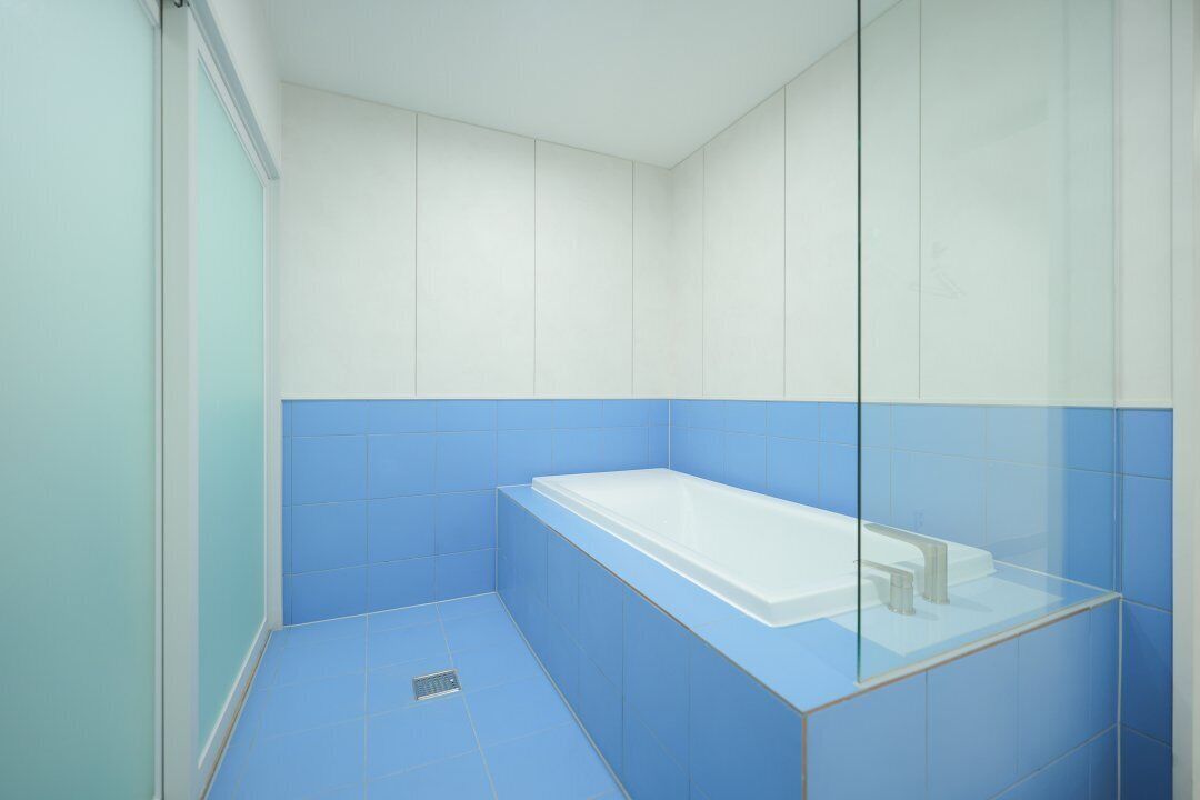 Un baño moderno con ducha envuelta en vidrio, una bañera blanca y paredes con azulejos azules.