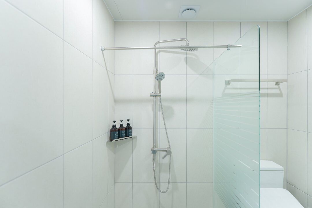 Un baño moderno con azulejos blancos, cabina de ducha de vidrio y un inodoro.