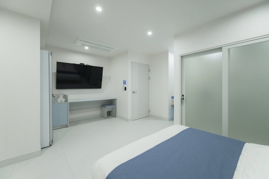A modern bedroom with a bed, a desk, a TV, and a wardrobe.