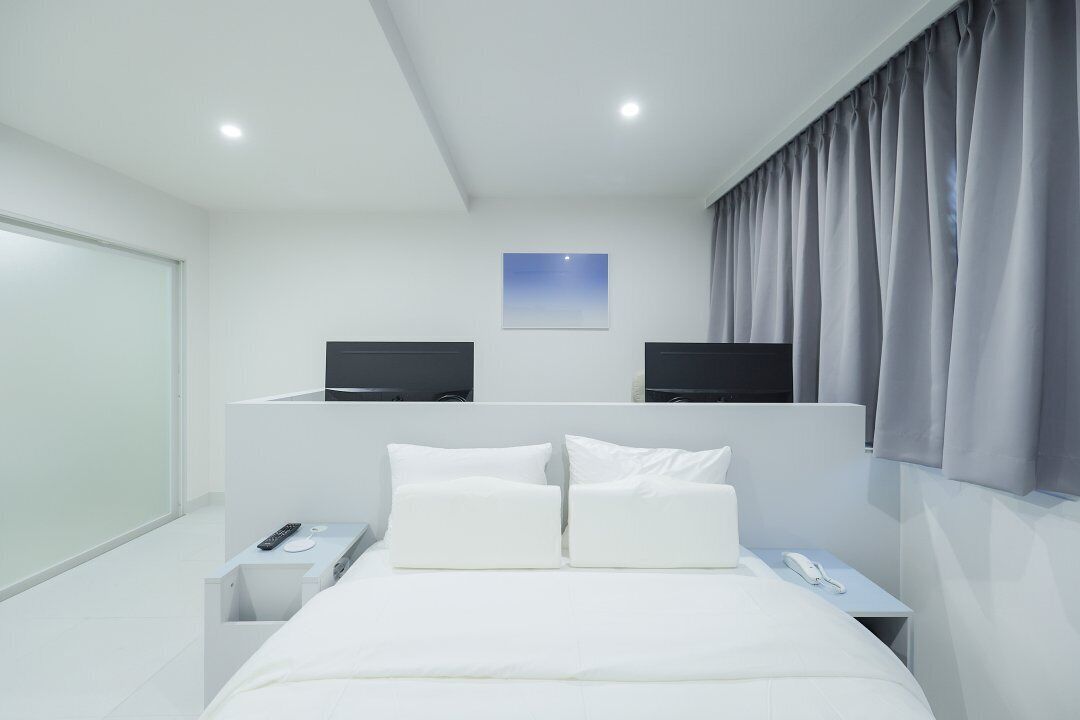Ett modernt hotellrum med en stor säng, två sängbord, en platt-TV på varje sängbord, ett litet sängbord med en telefon och ett fönster med gardiner.
