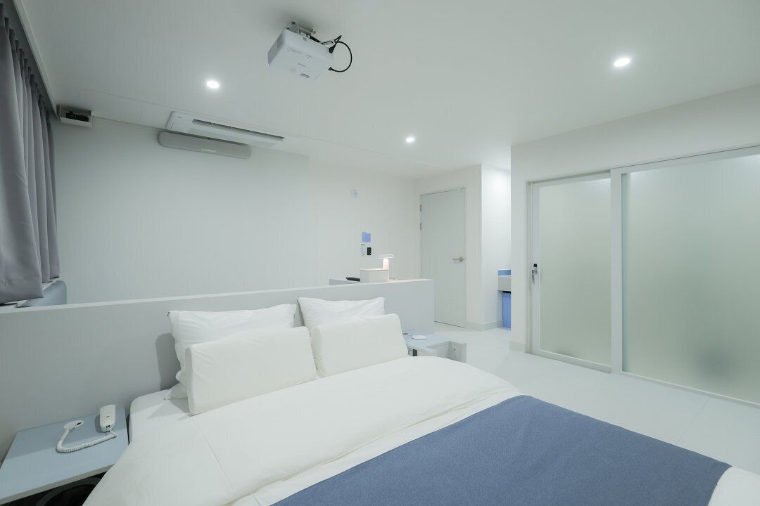 Een moderne hotelkamer met een groot bed, een bedtelefoon, een bureau met een lamp, en een schuifdeurkast.