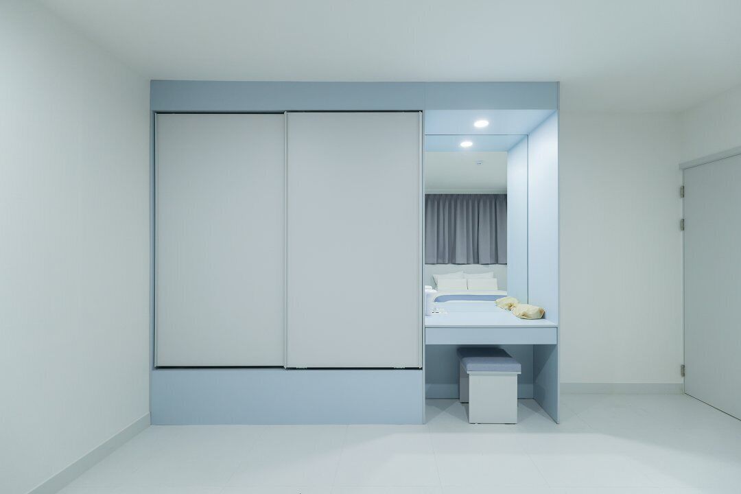 A modern bedroom with a large wardrobe, a bedside table, and a small trash bin.