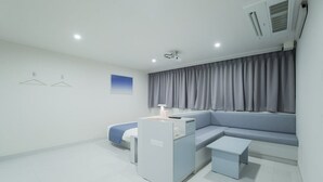 A modern, minimalist room with a grey sofa, a small table, and a desk with a lamp. - Anook Air Hotel Jinju (Jinju)