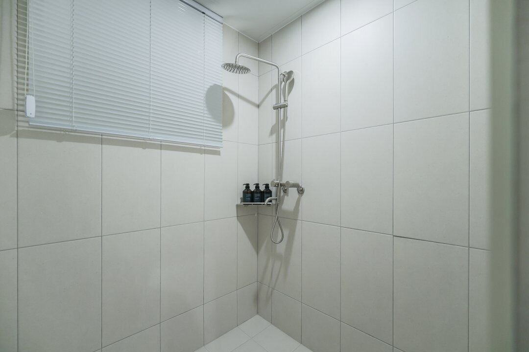A small, white-tiled shower room with a handheld showerhead and a wall-mounted faucet.