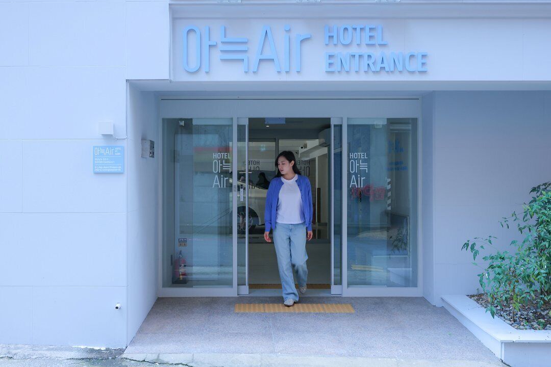 The entrance of a hotel named "Oh-Air" with a glass door and a small plant beside it.