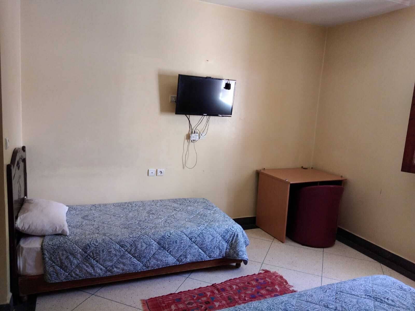 A small, simple room with a bed, a TV mounted on the wall, and a trash bin.