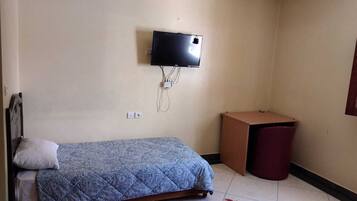 Una habitación pequeña y sencilla con una cama, un televisor montado en la pared y un cubo de basura.