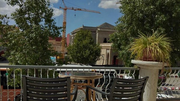 An outdoor seating area with two tables and four chairs, a potted plant, and a construction crane in the background. - Hotel Azaghar (M'rirt)