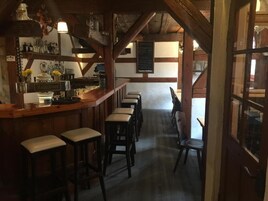 A rustic bar area with wooden beams, a bar counter, stools, and a chalkboard menu.