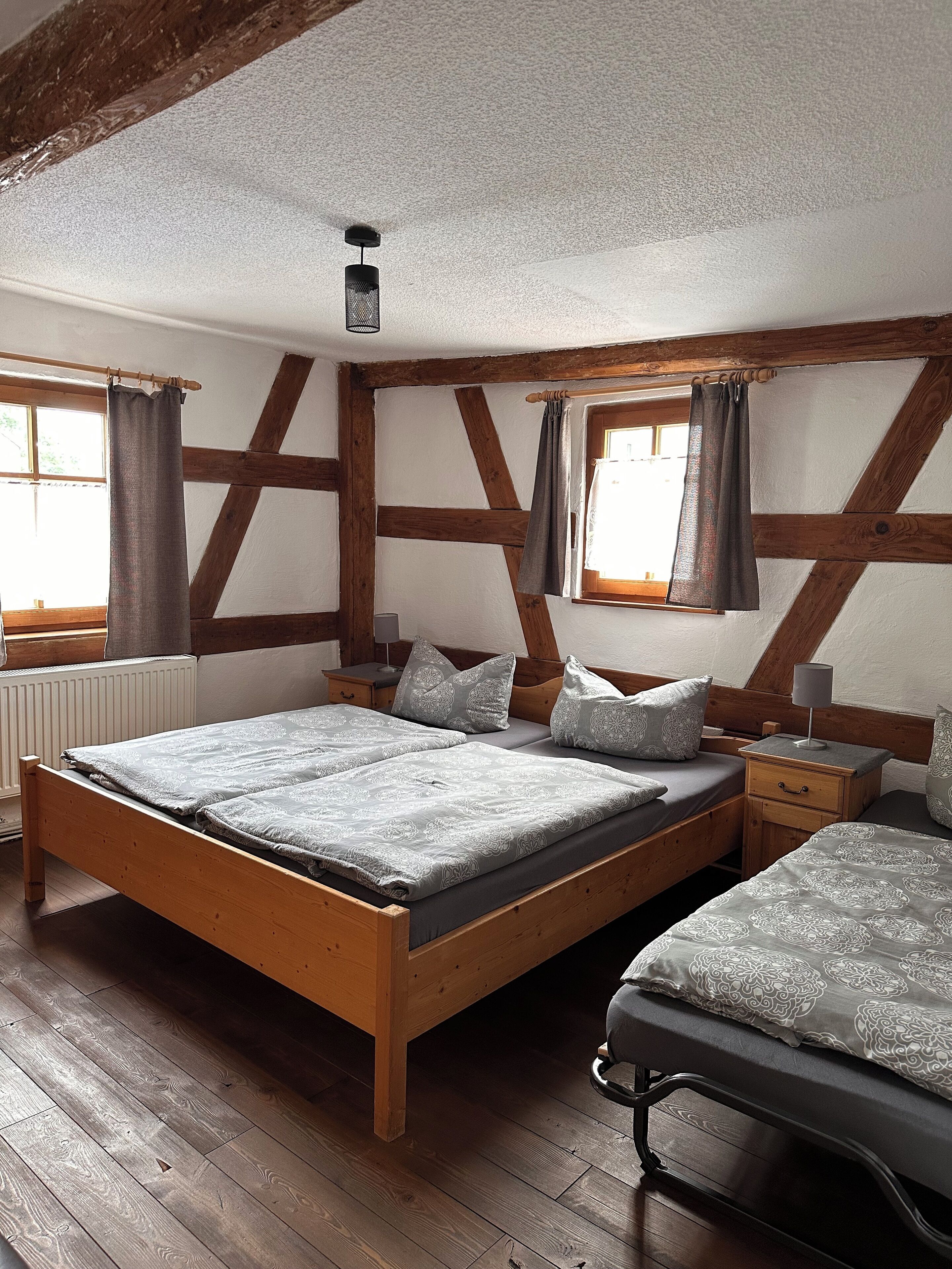 A bedroom with two beds, wooden beams, a window with curtains, and a radiator.