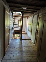 A narrow hallway with wooden doors on either side, a metal ladder, and a tiled floor.
