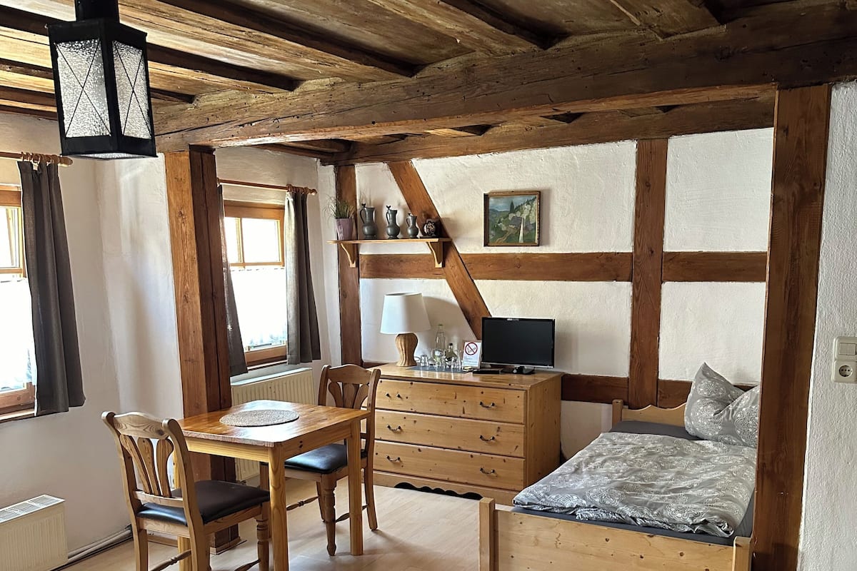 Una habitació acollidora amb un llit de fusta, un escriptori amb una cadira, una commode i una finestra amb cortines.