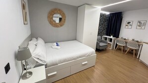 A modern bedroom with a bed, bedside table, and a desk area with chairs. - Modular Suites Alfonso Gomez (Madrid)