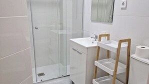 A modern bathroom with a glass-enclosed shower, a white sink with a mirror above, and a toilet with a wooden shelf. - Modular Suites Alfonso Gomez (Madrid)