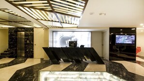 A modern lobby with a glass floor, a large screen displaying a guitar, and a television on the right. - Hotel Art Boutique (Hyderabad)