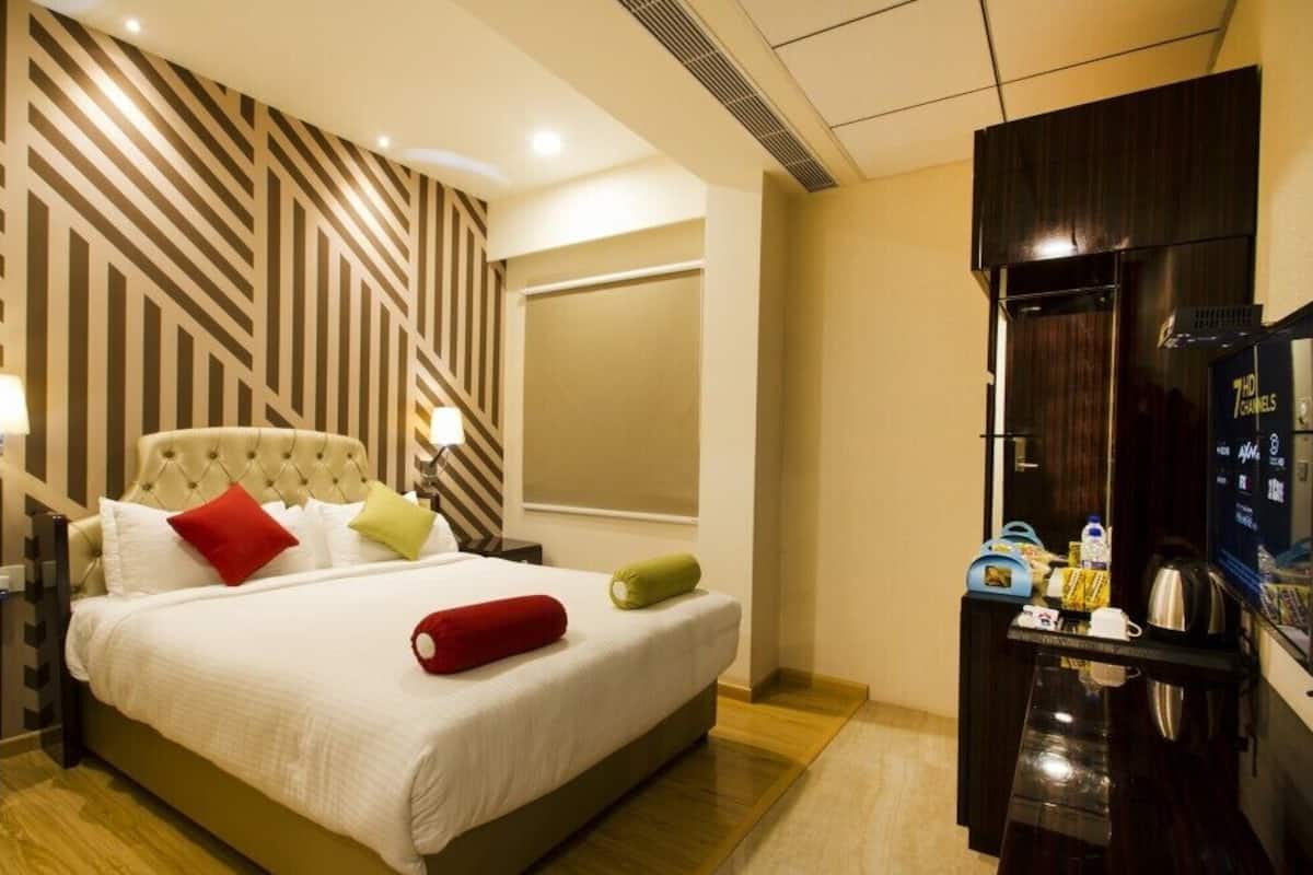 Una habitación de hotel con cama, televisión, minibar y un espejo grande.