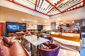 Un hall d’hôtel moderne doté d’un espace salon, d’un bar et d’un téléviseur diffusant un événement sportif.