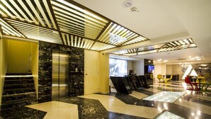 A modern lobby with a marble staircase, elevators, and a reception area with a glass partition. - Hotel Art Boutique (Hyderabad)