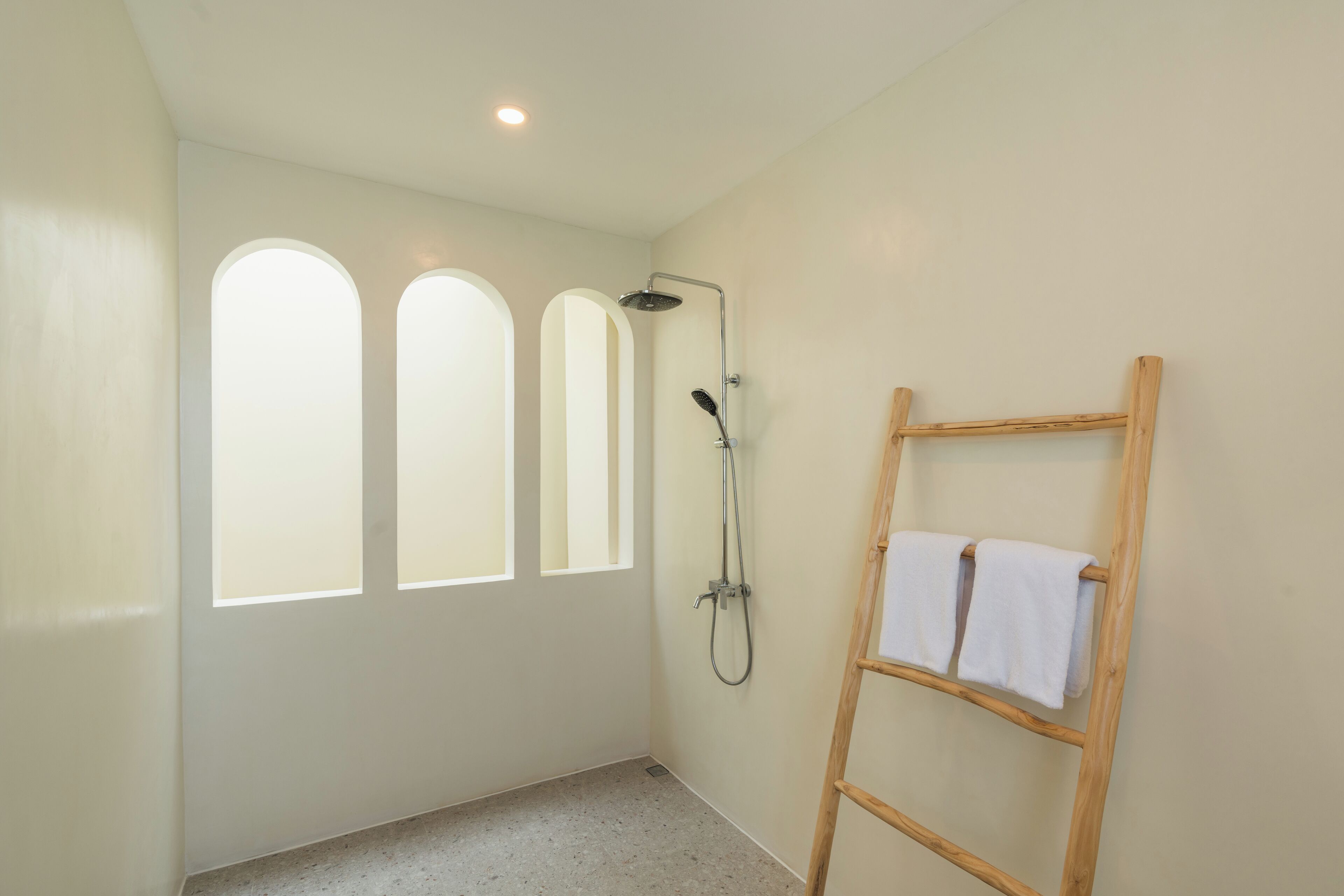 A bathroom with a shower, a wooden ladder, and three arched windows.