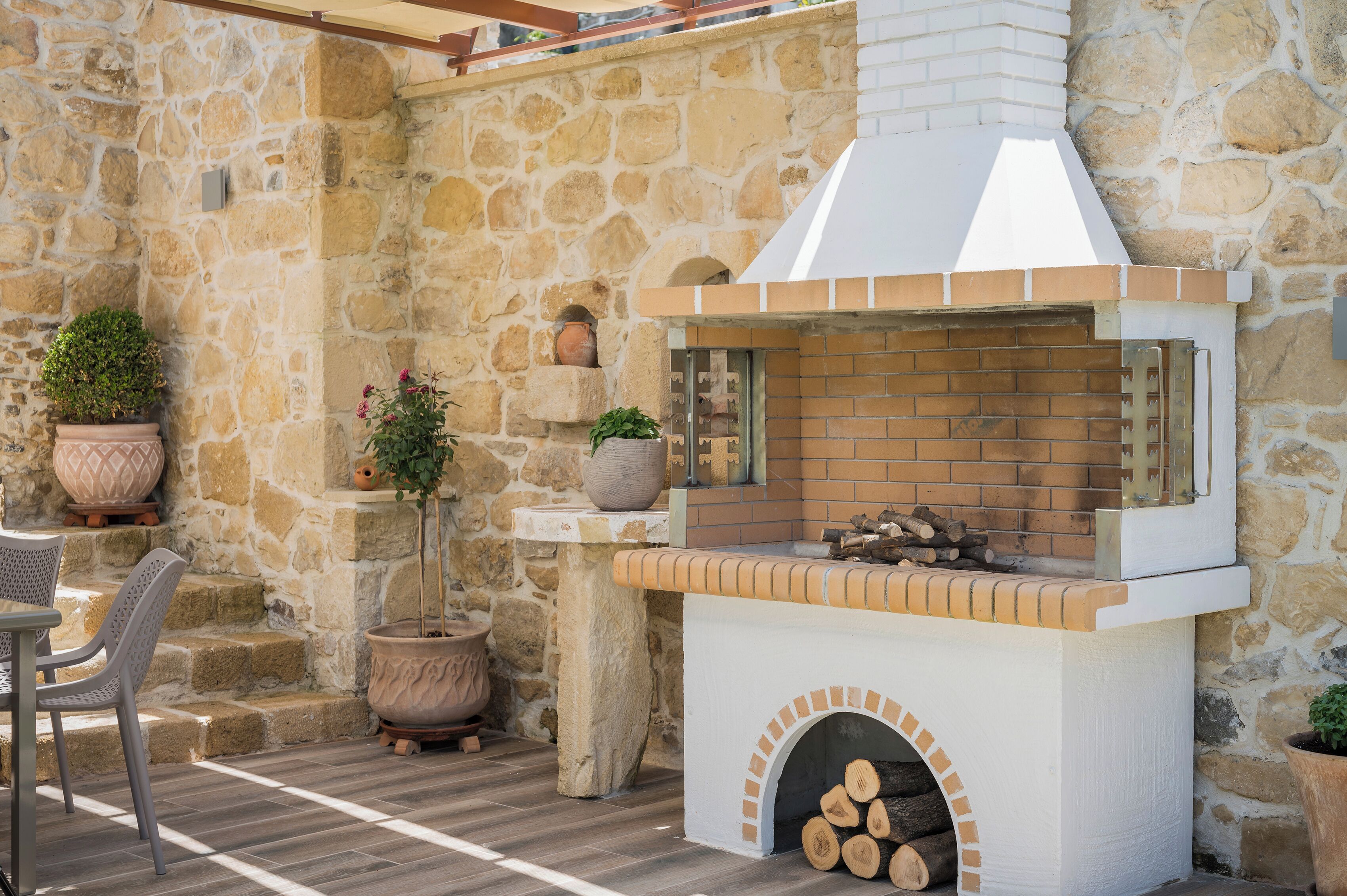 Pareda de pedra amb una llar de foc de rajola, seients exteriors i plantes en testos.