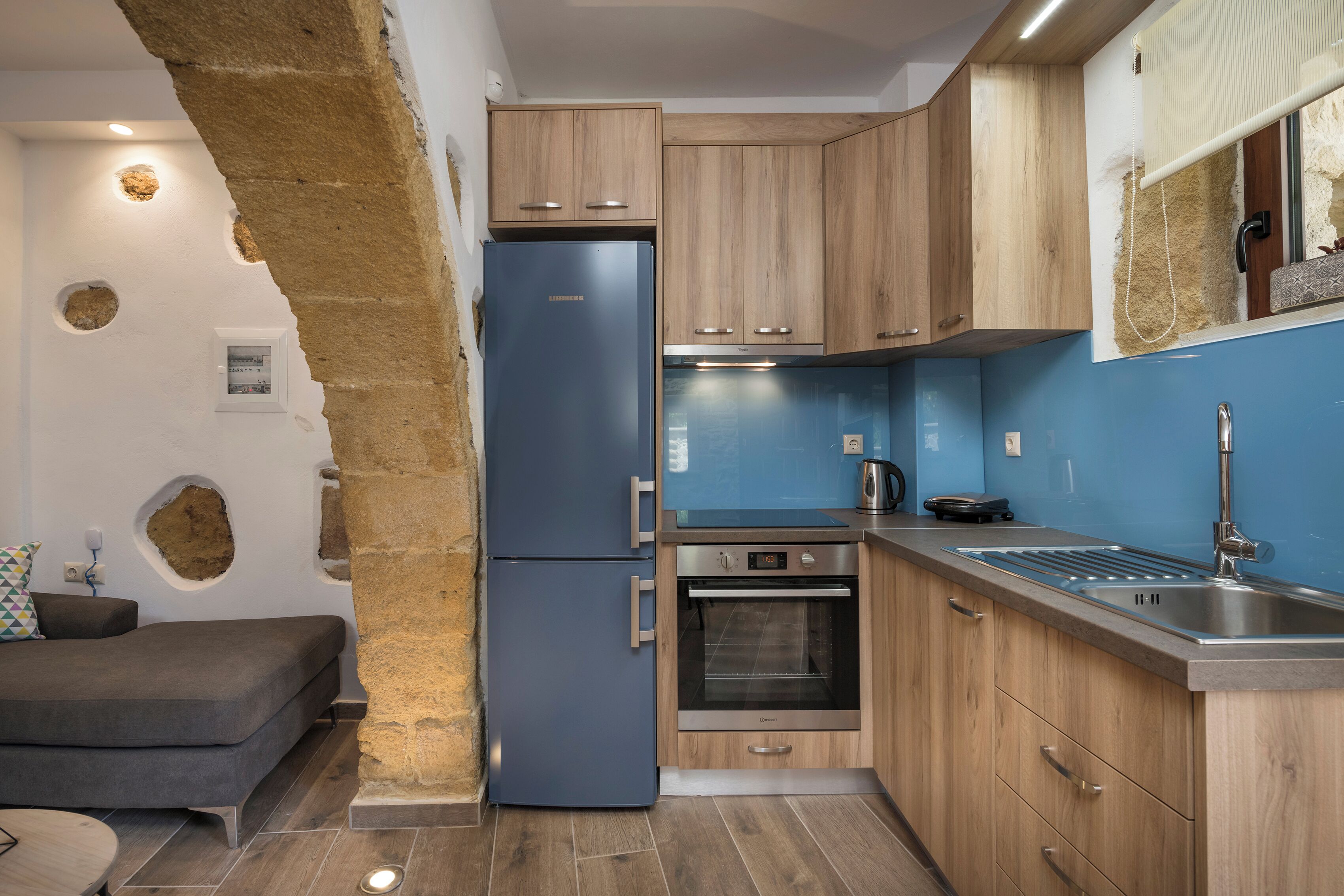 A compact kitchen with wooden cabinets, a blue refrigerator, a built-in oven, and a stainless steel sink.
