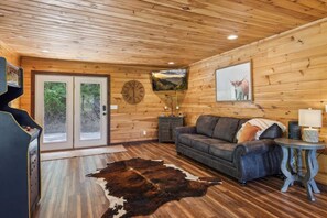 Interior de una cabaña de troncos con un sofá de cuero, techo de madera, un reloj y un cuadro con un ciervo.