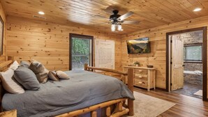Une chambre dans une cabane en bois, avec un lit, une commode, un téléviseur et un mur en pierre.