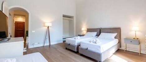 Habitación de hotel con dos camas, un escritorio y una silla. Hay dos lámparas de noche y un espejo grande en la pared.