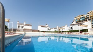 A swimming pool with a clear blue water surface, surrounded by white buildings with balconies and a clear sky above. - Gourmet in Grau i Platja (Gandia)