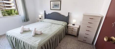 A bedroom with a bed, bedside tables, a dresser, a framed picture on the wall, and a window with curtains.