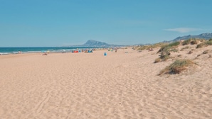 Une vaste plage de sable fin, un ciel dégagé, une montagne lointaine, ainsi que quelques personnes et des tentes.