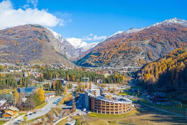 A town with a prominent circular building surrounded by mountains and autumn foliage. - Snow White in Bardonecchia (Bardonecchia)