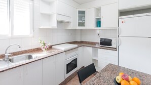 A modern kitchen with white cabinets, a granite countertop, a sink, a stove, a microwave, and a refrigerator. - Tallarol in Grau i Platja (Gandia)