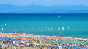 Een druk strand met talloze kleurrijke parasols en mensen die van het water genieten.