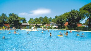A swimming pool with people swimming and playing, surrounded by trees and buildings. - Azzurro C2-6 in Bibione (San Michele al Tagliamento)