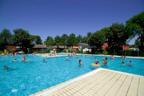 A swimming pool with people swimming and playing, surrounded by trees and buildings. - Azzurro C2-6 in Bibione (San Michele al Tagliamento)