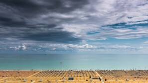 A beach with rows of sunbeds and umbrellas, a clear sky, and a calm sea. - Azzurro C2-6 in Bibione (San Michele al Tagliamento)