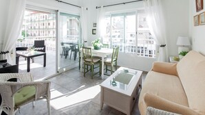 A bright living room with a sofa, a glass-top coffee table, and a dining area with chairs and a table. - Oreneta in Grau i Platja (Gandia)