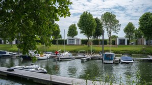 A marina with boats docked, a small building, and trees in the background. - Hikers Cabin in Maurik (Maurik)