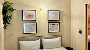 Un dormitorio con cama, mesita de noche, lámpara de pared y cuadros enmarcados.