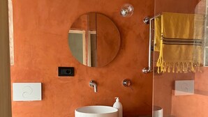 A bathroom with a round mirror, a white sink, a yellow towel, and a toilet. - Antica Dimora (Molfetta)