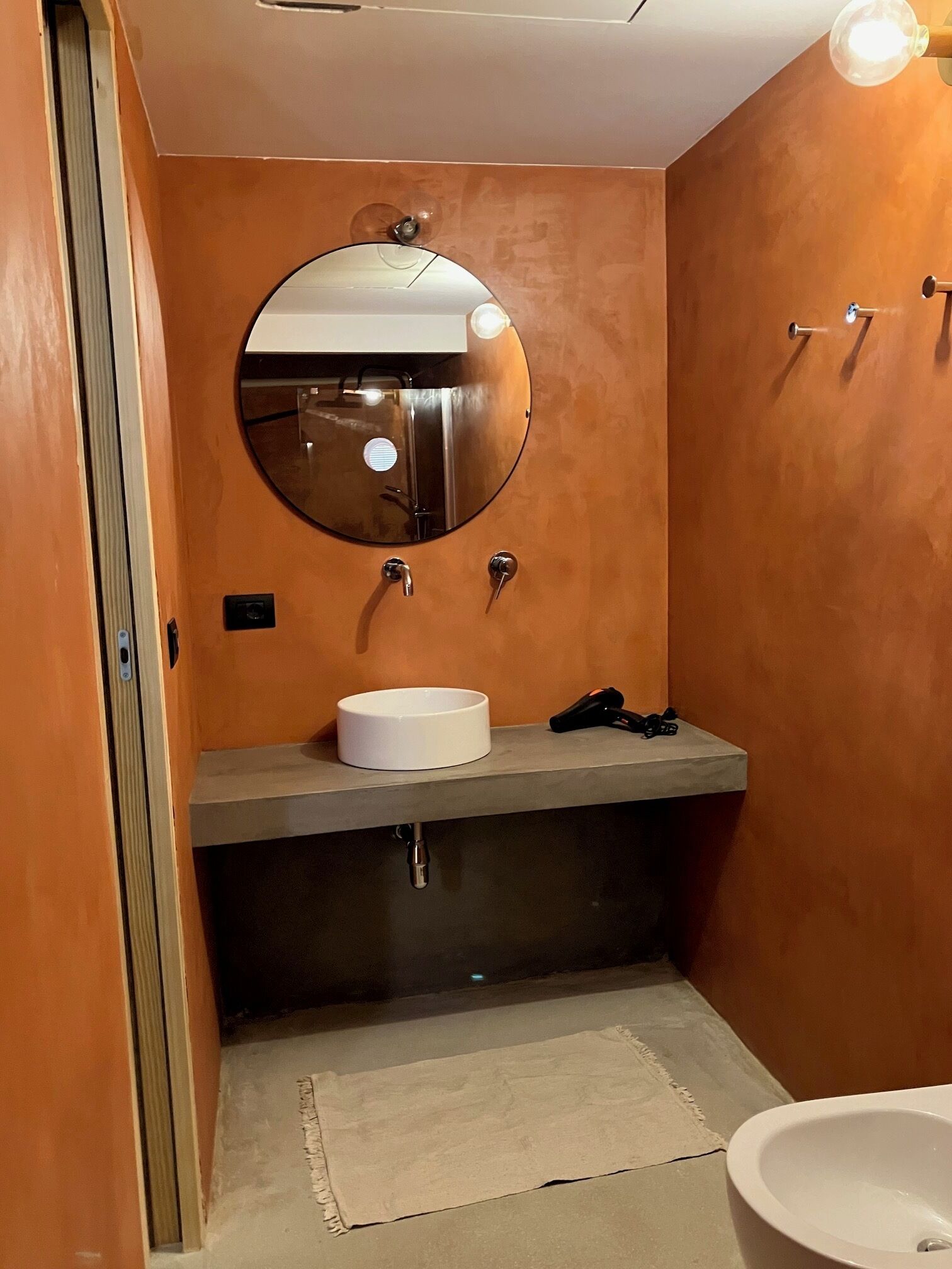 Une salle de bain avec un miroir rond, un lavabo blanc et des toilettes.