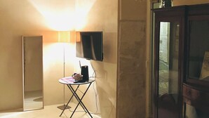Una habitación con techo curvo, una lámpara de pie, un televisor de pantalla plana, una pequeña mesa con una cesta y un mueble con espejo.