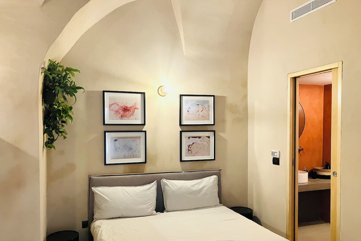 A bedroom with a bed, a nightstand, a wall-mounted plant, and framed artwork.