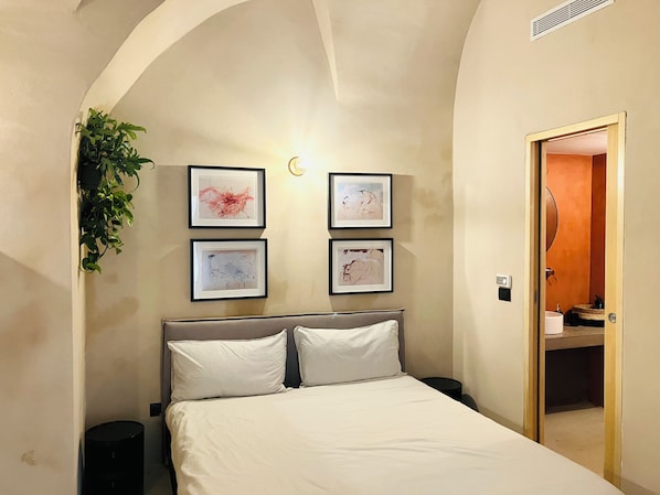 A bedroom with a bed, a nightstand, a wall-mounted plant, and framed artwork.
