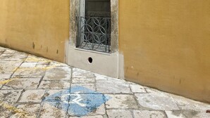 Un estrecho vano con una puerta de metal, una pequeña ventana encima y una flecha azul indicando la dirección en el suelo.